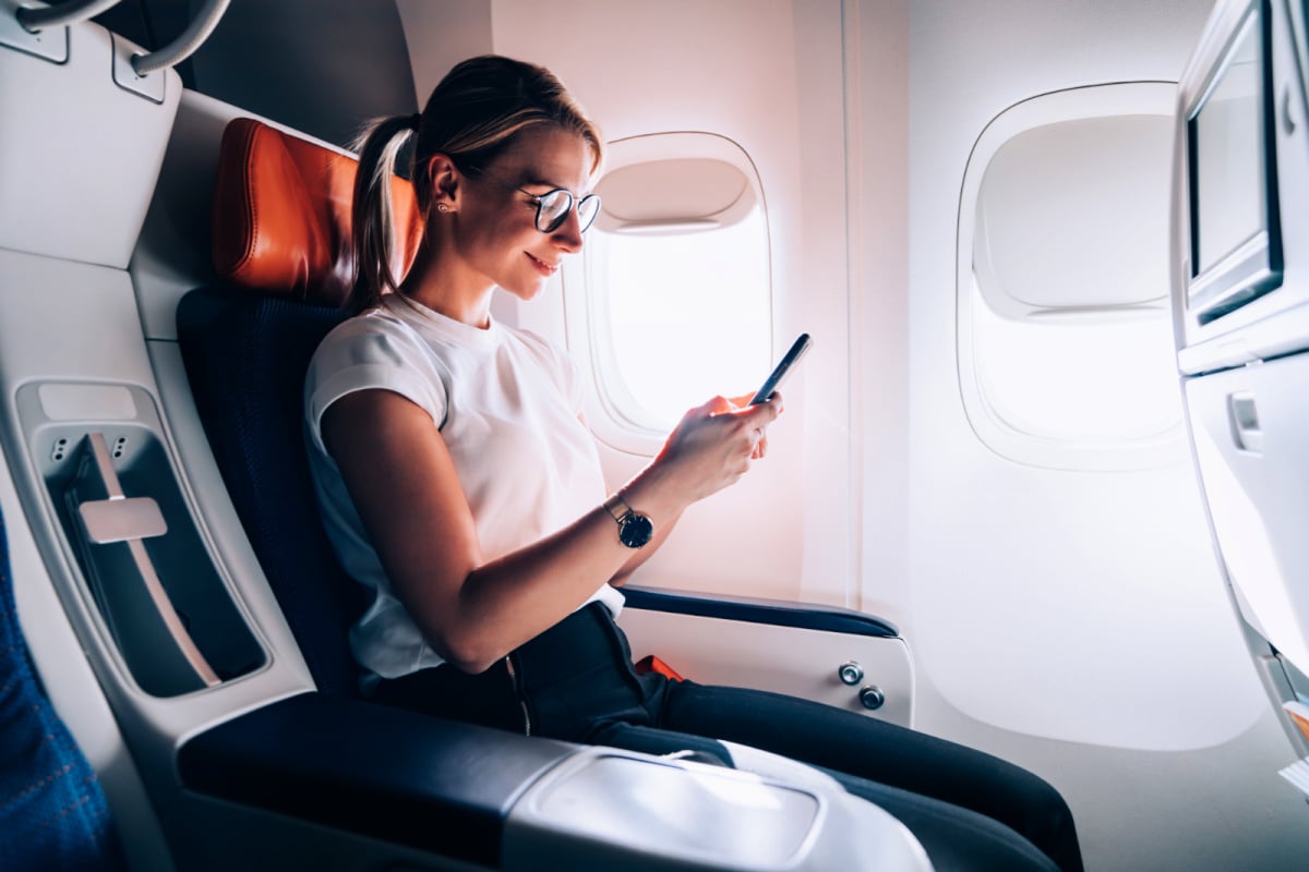 Woman on an airplane using Wifi on her phone